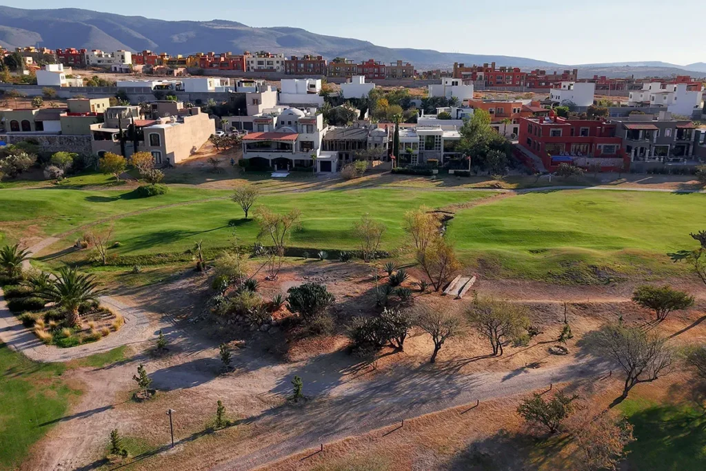 Sunset view over Club de Golf Malanquin in San Miguel de Allende, showing the golf course, trees, and surrounding residential homes.
