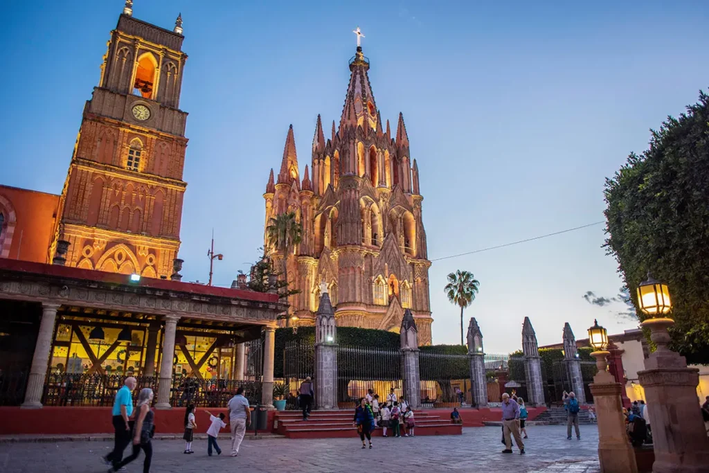 Evening view of the Parroquia de San Miguel Arcángel and the main plaza in Centro, with locals walking and gathering.
