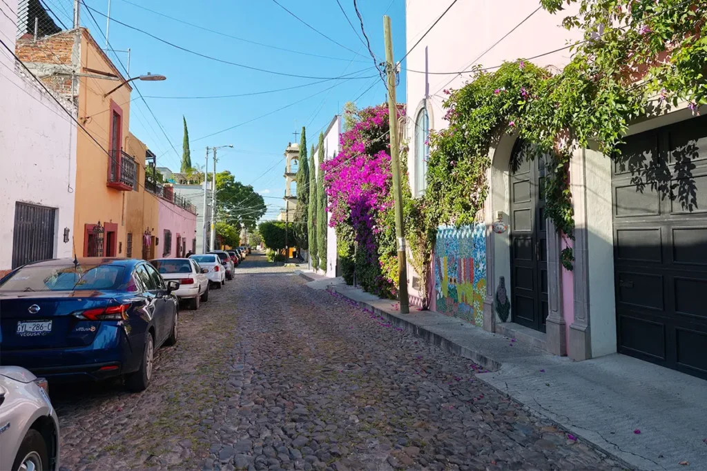Cobbled street in Guadalupe, San Miguel de Allende, with colorful homes, bougainvillea, and a church tower in the background.