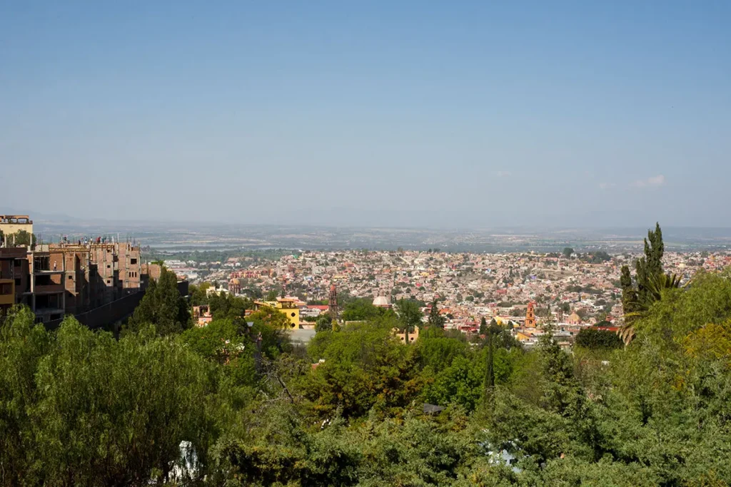 Panoramic view of San Miguel de Allende from Atascadero, showing hillside homes, greenery and the city skyline in the background.