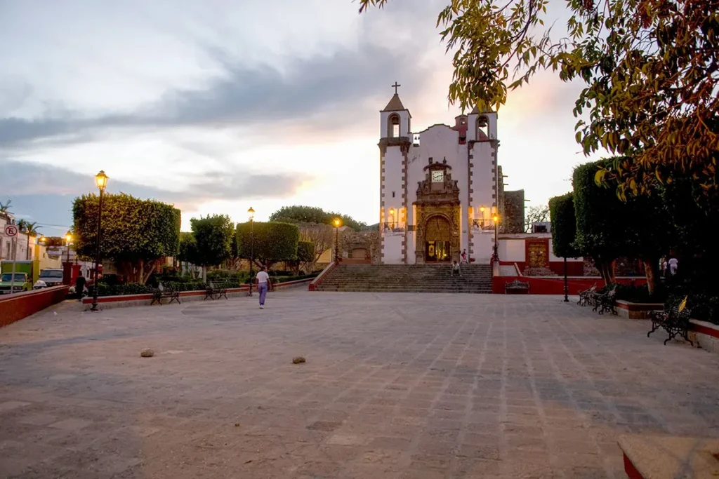 Parroquia de San Antonio at sunset, with a quiet plaza and trimmed trees in the San Antonio neighborhood of San Miguel de Allende.