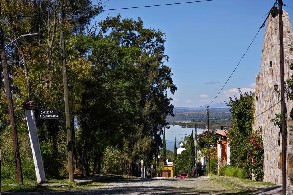 Cobblestone street in Los Frailes neighborhood, San Miguel de Allende, with lake views, mature trees, and colonial stone buildings along a quiet residential road.