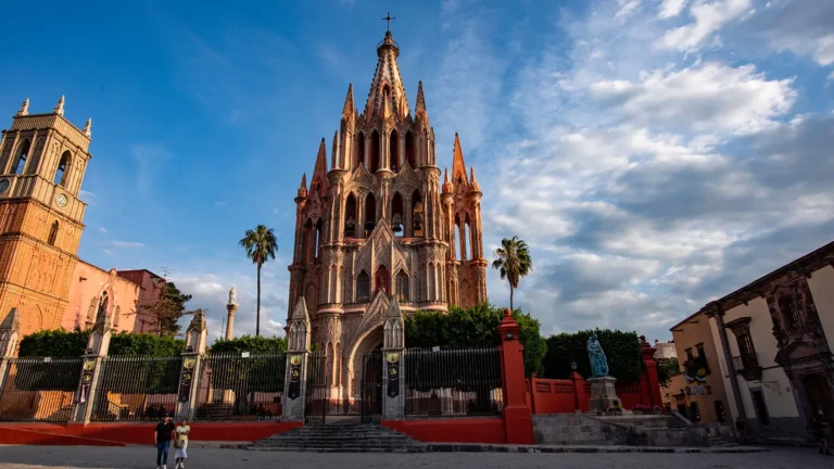 Things-to-Do-in-San-Miguel-de-Allende-A-First-Timers-Guide - Colonial Real Estate - Colonial Real Estate Parroquia de San Miguel Arcangel rising above the main plaza in San Miguel de Allende, Guanajuato, with its distinctive pink limestone neo-Gothic facade and colonial buildings surrounding El Jardin
